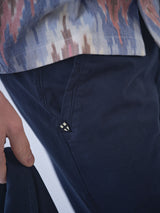 A close-up of a person wearing Blue de Gênes BGmenzino Vecchio Shorts in Dark Navy with a patterned shirt in blue, beige, and orange. The person holds a dark item in their left hand, with pocket and waistband detail visible.
