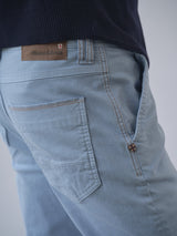 Close-up of the BGpaulo Pavia Pant - Blue Fog by Blue de Gênes, featuring light blue cotton stretch denim, a brown leather brand patch above the pocket, a small cross emblem near the stitching, and paired with a navy sweater.