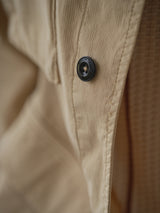 Close-up of pale khaki corduroy fabric with a black button engraved with subtle text, highlighting the ribbed texture of the Blue de Gênes BGhunter Vecchio Jacket.