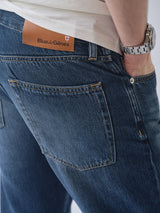 Wearing BGmarco Rowan Jeans - Used by Blue de Gênes—relaxed fit, classic 5-pocket style with a leather label—a person in a white shirt has one hand in their back pocket and wears a silver wristwatch.