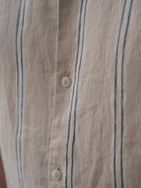 Close-up of the BGcody Fling Shirt in Pale Khaki by Blue de Gênes, a relaxed fit linen shirt with beige fabric, vertical blue stripes, and white buttons.