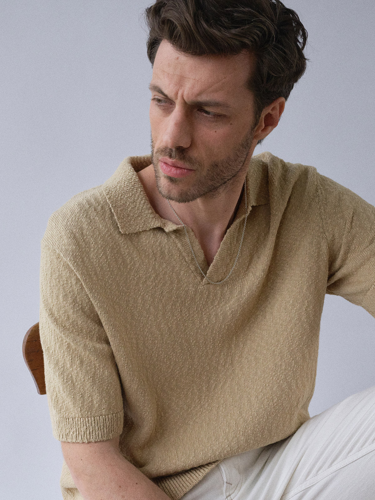 A man with short brown hair and light stubble wears the Blue de Gênes BGjohn Slubby Polo in Pale Khaki and light pants, gazing thoughtfully to his left against a plain light background.