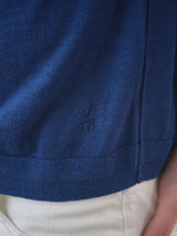 A close-up of a person wearing the BGmonty Knit - Navy Peony shirt by Blue de Gênes, featuring an embroidered shield emblem near the hem, with off-white pants visible below.