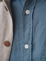 Close-up of a blue button-up shirt partly covered by the BGjazzy Ola Jacket in Dark Sand from Blue de Gênes, featuring brown buttons.