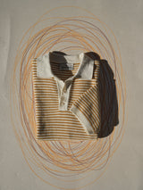 The BGbob Knit Polo - Sunflower by Blue de Gênes, a cotton short-sleeve shirt with a white collar and cuffs plus a brown and white geometric pattern, is neatly folded on a flat surface surrounded by hand-drawn circular lines.