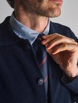 A man adjusts the Nekutaki Tie #B - Navy Stripe by Blue de Gênes, paired with a textured navy jacket and blue striped shirt. Only his lower face and upper body are shown, showcasing these timeless mens fashion accessories.