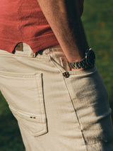 A person outdoors on grass wears the Blue de Gênes BGwally Diamond Polo in Coral with cream jeans, one hand in their pocket and a watch visible on their left wrist. Sunlight highlights the scene.