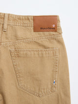 Close-up of the back pocket of tan BGgiacomo Color Jeans - Tanin by Blue de Gênes, showing rigid denim, a brown leather Blue de Gênes patch on the waistband, and a small blue and white tag on the pocket.