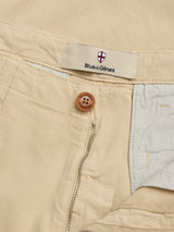 Close-up of BGpalco Rodas Pants in pale khaki by Blue de Gênes, with a relaxed regular fit, visible zipper, brown button, and the brand's shield logo label sewn inside the waistband.