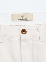 Close-up of the waistband on Blue de Gênes BGpalco Twill Pants in Chalk, men's relaxed fit cotton twill with a brown button, belt loops, and a label beneath a small crest featuring a red cross.