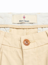 Close-up of BGcopple Rodas Shorts in pale khaki by Blue de Gênes, featuring a cotton-hemp blend, brown button, pleat front details, and a branded label with crest and red cross inside the waistband.