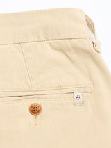 Close-up of the back pocket of BGcopple Rodas Shorts in Pale Khaki by Blue de Gênes, made from a cotton-hemp blend with a wooden button, stitched flap, and a white tag featuring a red and blue shield emblem on the right side.