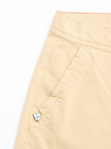 Close-up of Blue de Gênes BGmenzino Vecchio Shorts in Pale Khaki, featuring a casual fit, visible waistband, side pocket, and a small shield-shaped metal emblem near the pocket against a white background.