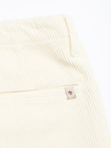 Close-up of BGfloyd Cord Shorts - Chalk by Blue de Gênes: soft cream-colored cotton corduroy with an elastic waistband, loose fit, zippered back pocket, and a small tag featuring a red and blue shield emblem.