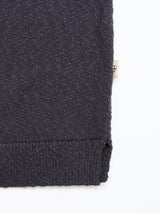 Close-up of the corner of a dark navy BGjohn Slubby Polo by Blue de Gênes, featuring knitted fabric and a stitched hem. A small beige tag with a red and white shield emblem is visible on the side against a white background.