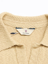 Close-up of the BGjohn Slubby Polo in Pale Khaki by Blue de Gênes, featuring a textured cotton knit and an inside collar label with the brand’s shield logo, capturing classic vintage leisurewear style.