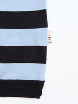 A close-up of the BGwally Stripe Polo - Dark Navy by Blue de Gênes, featuring alternating black and light blue stripes and a small beige tag with a red cross emblem on the side seam, set against a white background.