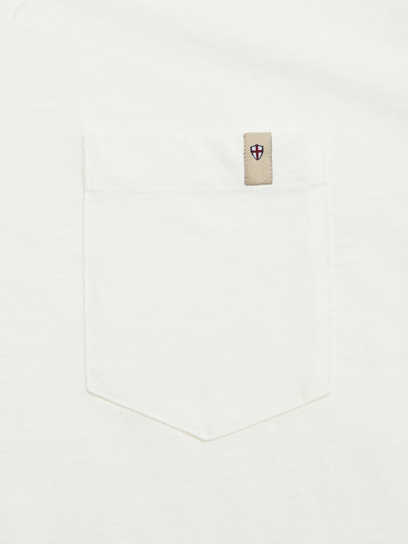 Close-up of Blue de Gênes BGoscar T-Shirt - Snow Fall’s white crewneck and pocket, with a beige tag above featuring a shield emblem with a red cross and blue border. Made from 100% cotton.