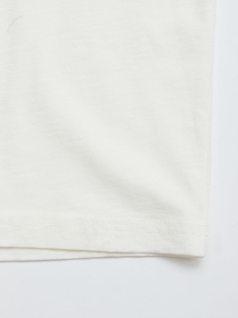 Close-up of the bottom edge of the Blue de Gênes BGoscar T-Shirt - Snow Fall, a plain white 100% cotton crewneck, showcasing fabric texture, stitching, and hem details against a white background.