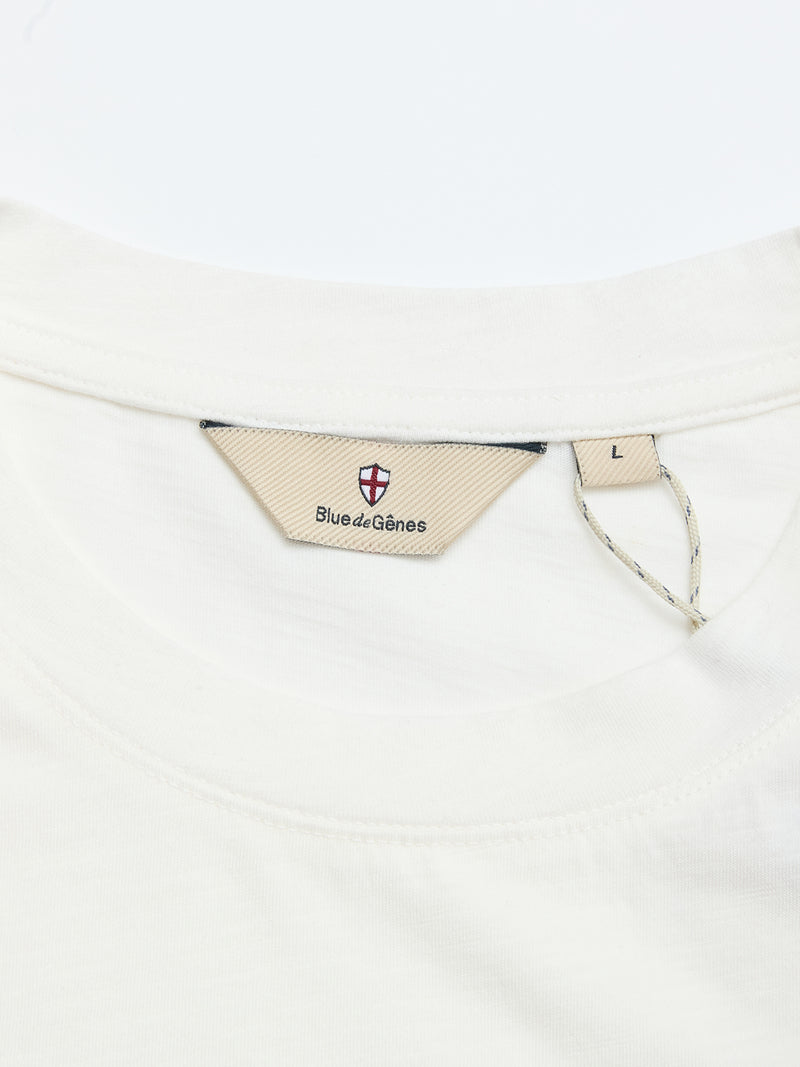 Close-up of the BGoscar T-Shirt - Snow Fall by Blue de Gênes: white cotton, regular fit, beige label with a red and white crest and "Blue de Gênes" text at neck, plus an L size tag attached with a string.