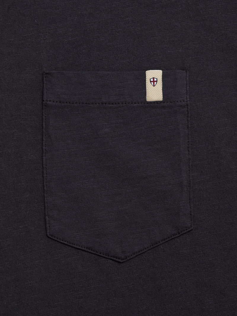 A close-up of the BGoscar T-Shirt - Jet Black by Blue de Gênes shows its dark 100% cotton fabric and shirt pocket with a small white tag featuring a red shield emblem, ideal for classic or casual crewneck styles.