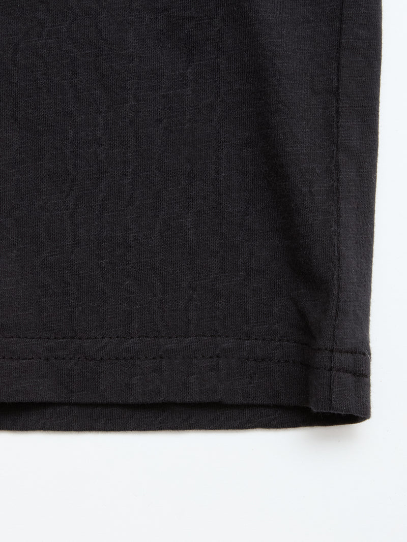 Close-up of the bottom hem of a Blue de Gênes BGoscar T-Shirt in Jet Black, made from 100% cotton, highlighting stitching details and fabric texture against a white background.