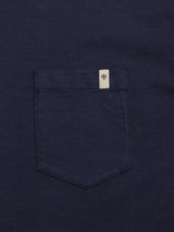 A close-up of the Blue de Gênes BGoscar T-Shirt in dark navy, made from 100% cotton, showing its chest pocket with a cream tag and a red-and-blue shield emblem stitched at the top edge.