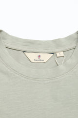 Close-up of the BGoscar T-Shirt in Shadow Green by Blue de Gênes, featuring a crewneck style, inner label with branding and shield logo, size L tag, and soft 100% cotton fabric with a subtle texture.