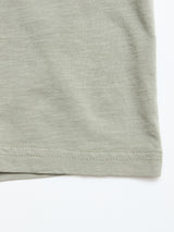 Close-up of the hem of the BGoscar T-Shirt in Shadow Green by Blue de Gênes, a soft 100% cotton crewneck with subtle texture, lying flat on a white background. The bottom edge stitching is clearly visible.