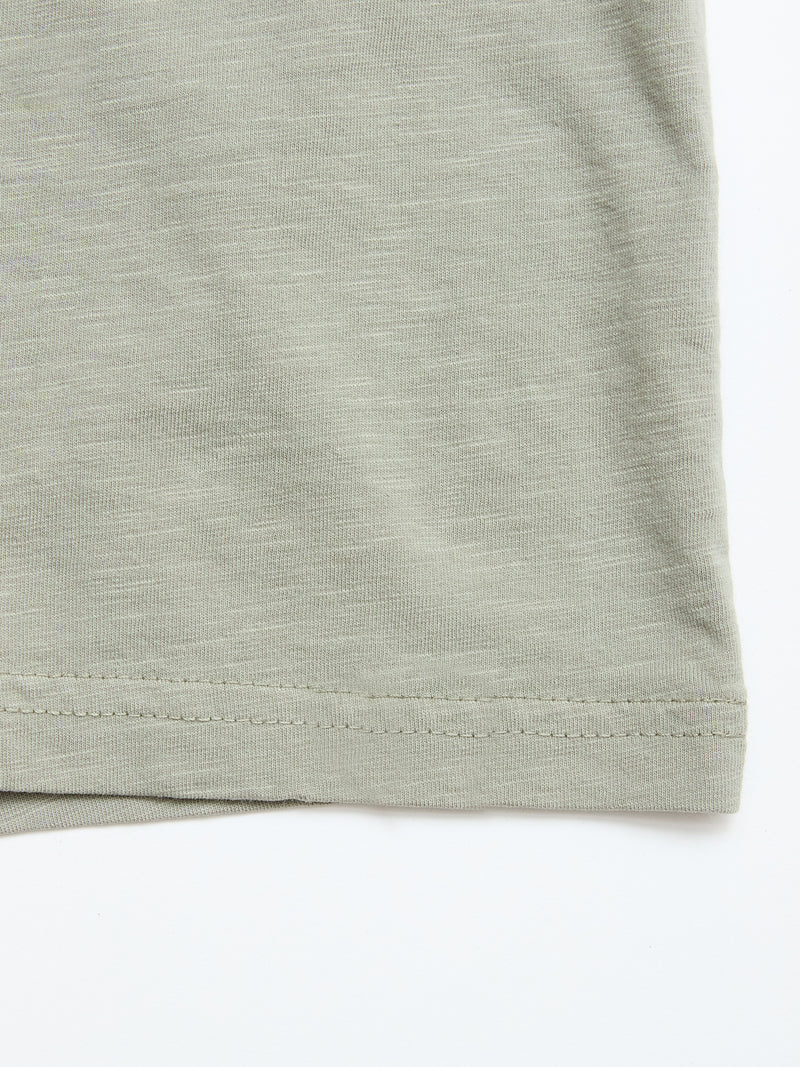 Close-up of the hem of the BGoscar T-Shirt in Shadow Green by Blue de Gênes, a soft 100% cotton crewneck with subtle texture, lying flat on a white background. The bottom edge stitching is clearly visible.