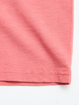 Close-up of the hem of a coral slub cotton fabric, highlighting detailed stitching and texture. The Blue de Gênes BGoscar T-Shirt is neatly folded at the bottom right corner on a white background.