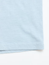 Close-up of the bottom hem of the Blue de Gênes BGoscar T-Shirt - Blue Fog, a 100% cotton crewneck, showcasing stitching and fabric texture against a white background.