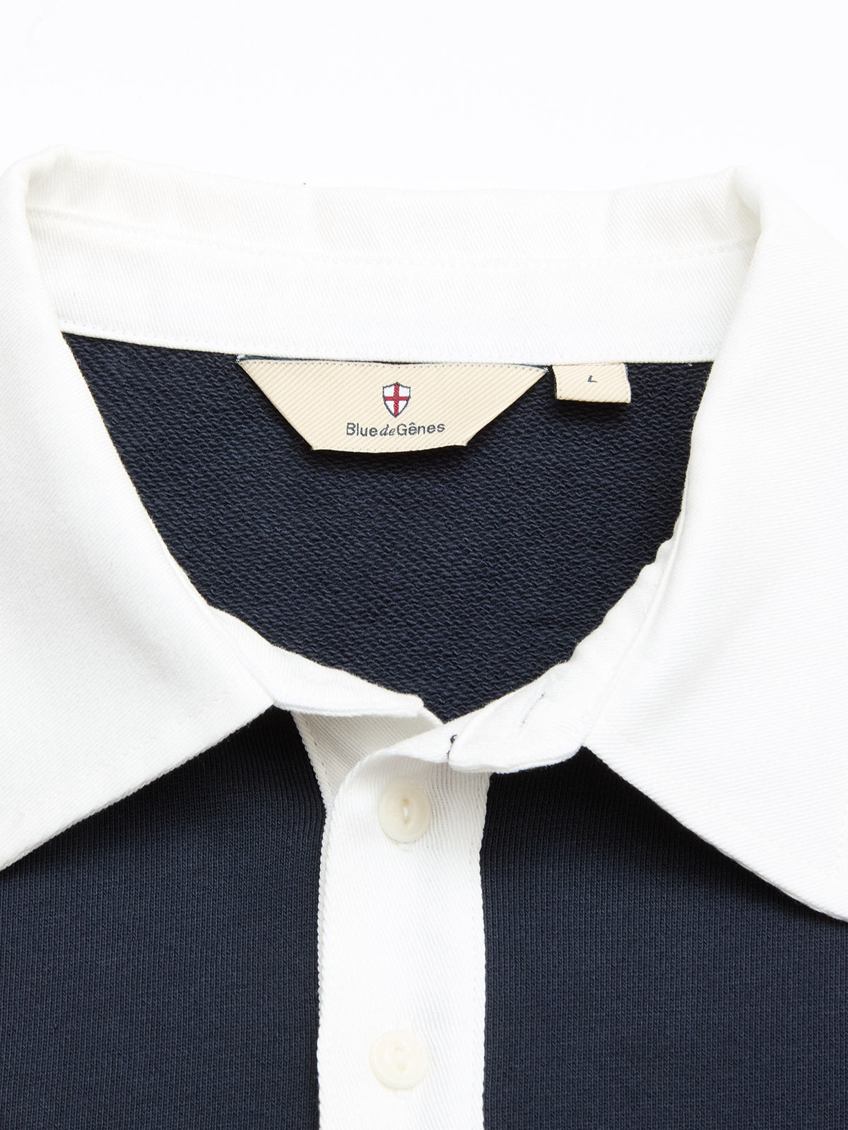 A close-up of the BGclubhouse Rugby Sweatshirt - Navy by Blue de Gênes in soft cotton jersey, featuring a white collar and buttons. The Blue de Gênes label and L size tag are stitched inside the collar.