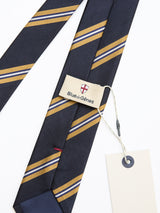 The BGponsy Tie - Dark Navy by Blue de Gênes is a men's silk necktie in navy with diagonal gold and white stripes, shown with branded and blank cream tags on a white background.