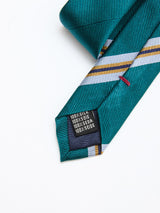 A close-up of the BGponsy Tie - Green by Blue de Gênes, featuring green stripes and a black label with "100% Silk" in four languages, lying on a white surface—a timeless men's fashion accent.