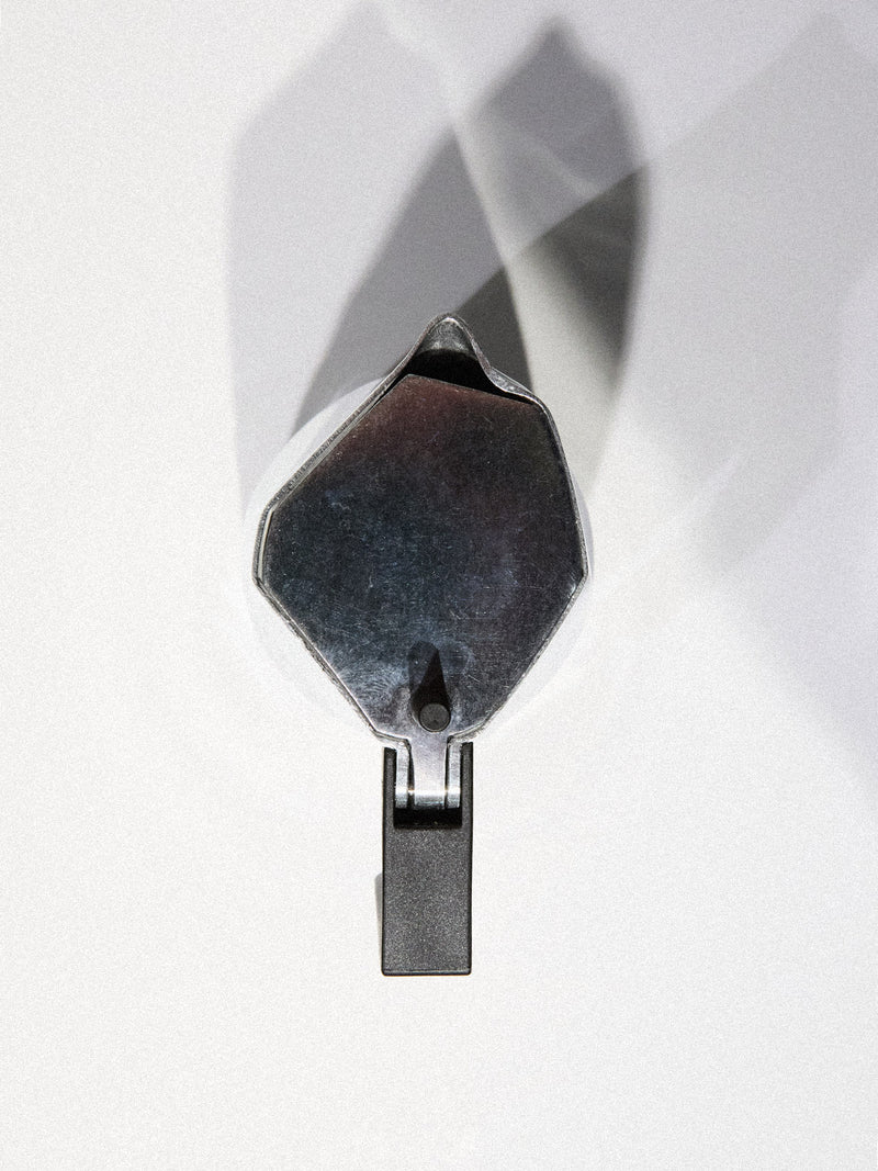 A grey BDG Coffee Maker by Blue de Gênes rests on a white surface, its sleek form casting a clear shadow behind it. The coffee maker stands upright, handles pointing down.