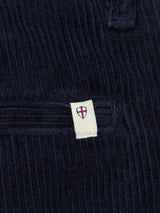 Close-up of Blue de Gênes BGfloyd Cord Shorts in Dark Navy, showing a beige tag with a shield emblem and red cross by the pocket seam—highlighting the premium detail on these loose fit corduroy shorts.