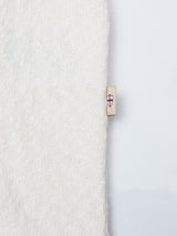 A close-up of the BGjohn Slubby Polo in Chalk by Blue de Gênes shows its textured, off-white knit and a small beige tag with a red and blue shield emblem on the right edge, set against a plain white background.