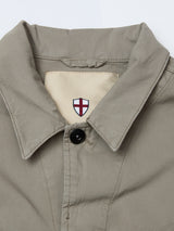 A close-up of the BGhunter Vecchio Jacket in Shadow Green by Blue de Gênes, featuring a single black button and a cream label with a red and white shield emblem inside the collar.