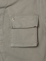 Close-up of a BGhunter Vecchio Jacket in Shadow Green by Blue de Gênes, showing a pocket with a flap and a small round pin with a white background and red cross on the upper left corner.