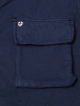 A close-up of a pocket with flap on the Blue de Gênes BGhunter Vecchio Jacket in Dark Navy, showing a white shield patch with a red cross on the upper left corner.