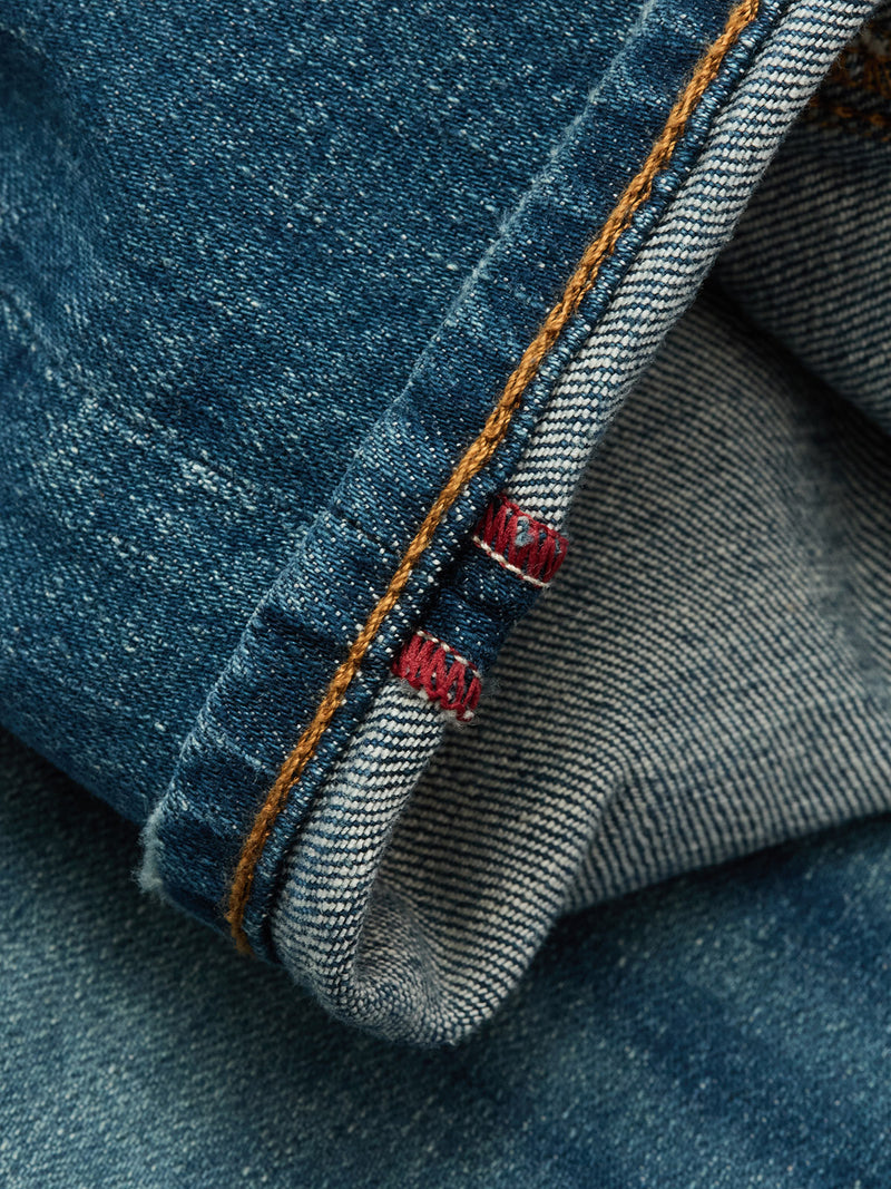 A close-up of Blue de Gênes Vinci Topaz Vintage Jeans - Used, made in Italy, showing the folded cuff with orange stitching and red bar tacks. The comfort stretch denim’s texture and weave are clearly visible.