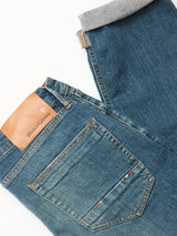 A pair of Vinci Topaz Vintage Jeans - Used by Blue de Gênes in blue comfort stretch denim, regular fit, with visible back pocket stitching, a brown leather Blue de Gênes label, and one cuffed leg revealing gray inner fabric on a white background.