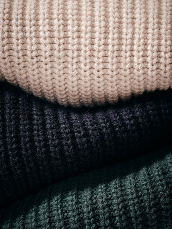 Close-up of three Yomaha Halfzip Knit sweaters by Blue de Gênes—shown in light beige, dark navy, and scarab green. The chunky knit texture highlights their cozy, classic appeal.