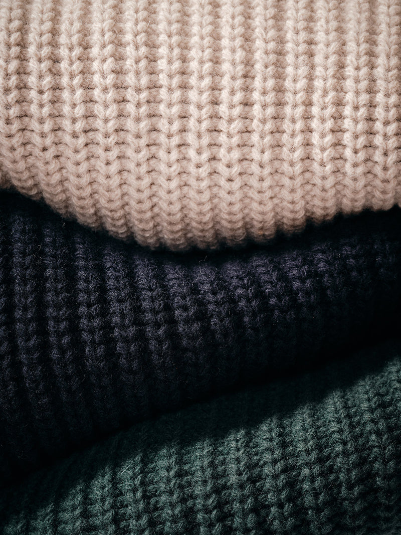 Close-up of three Yomaha Halfzip Knit sweaters by Blue de Gênes—shown in light beige, dark navy, and scarab green. The chunky knit texture highlights their cozy, classic appeal.