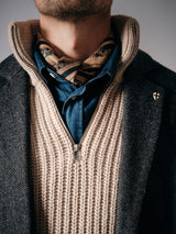 A close-up of a person wearing a grey jacket, cream zipped knit sweater, blue denim shirt, and the Blue de Gênes Siruku Scarf - Mixed Colours tied at the neck. Their face is not shown.