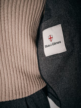 Close-up of a person wearing the Fukui Blazer - Black Pattern by Blue de Gênes with a beige ribbed sweater, highlighting a white sleeve patch with red shield and black text for a relaxed yet workwear-inspired style.