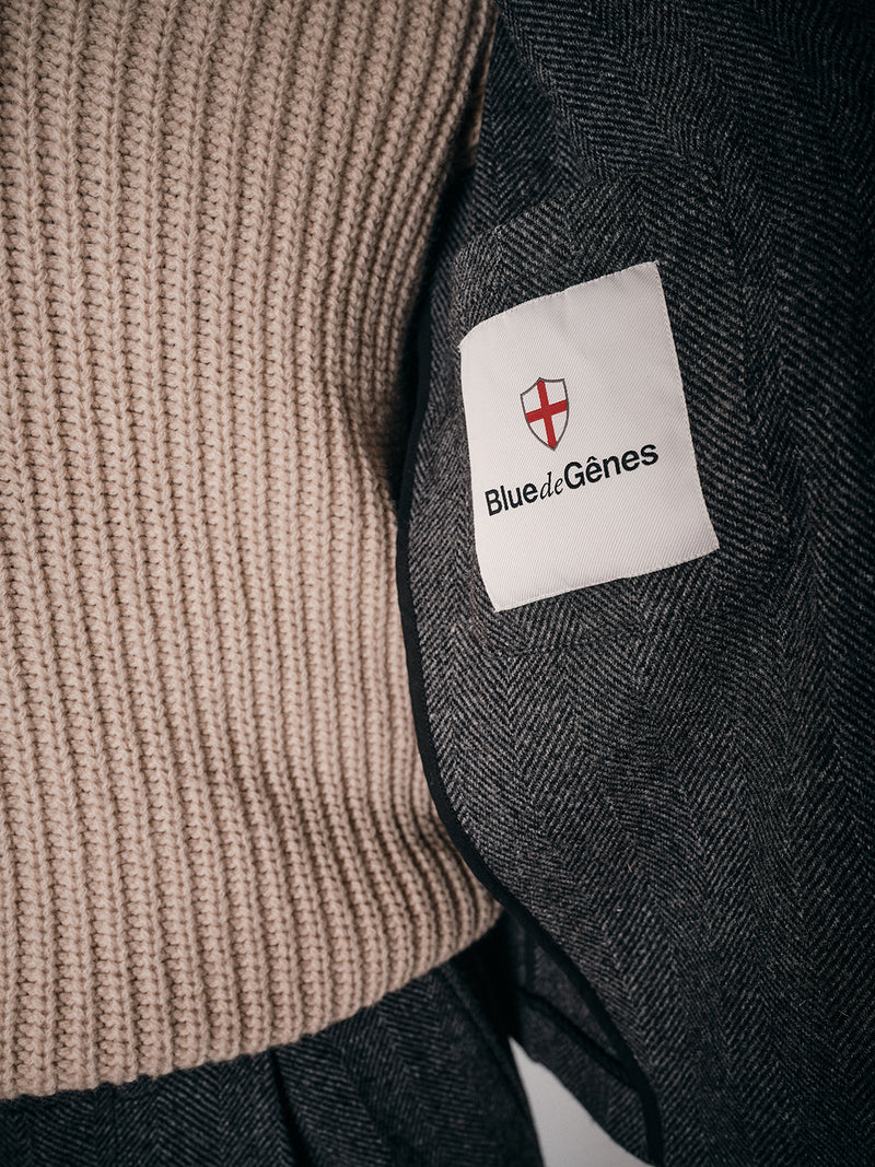 Close-up of a person wearing the Fukui Blazer - Black Pattern by Blue de Gênes with a beige ribbed sweater, highlighting a white sleeve patch with red shield and black text for a relaxed yet workwear-inspired style.
