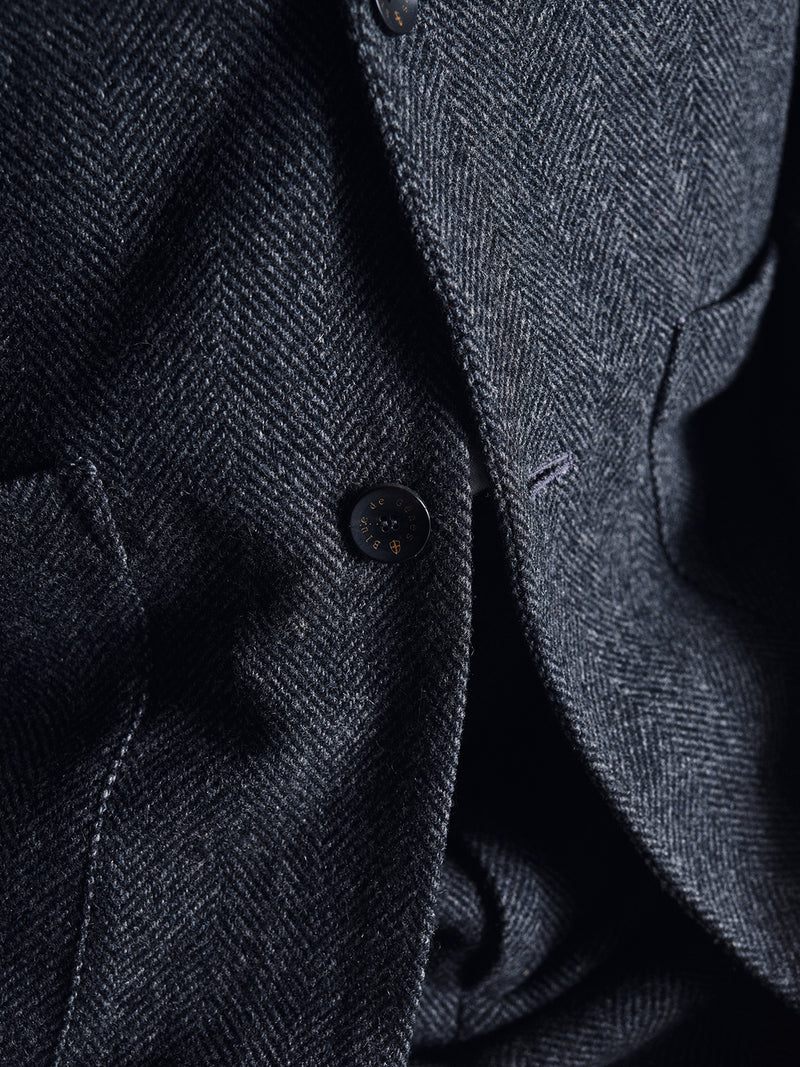 Close-up of the Fukui Blazer - Black Pattern by Blue de Gênes, showcasing relaxed tailoring details—a button, lapel, and pocket—with the texture and herringbone weave of this workwear jacket clearly visible.