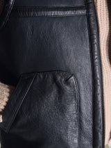 Close-up of the Blue de Gênes Saga Shearling Gilet - Scarab, highlighting the texture of German Merino sheepskin, a visible zipper, and a beige knitted sweater sleeve.